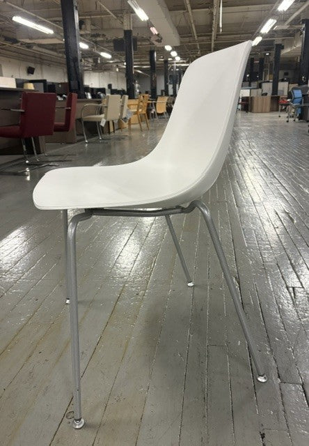 A modern white molded plastic chair with a chrome metal four-leg base, photographed in a warehouse or showroom setting with a polished wood floor.