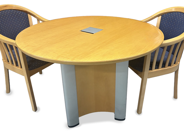 An oval wood conference table with a light oak finish and silver pedestal legs, shown with two matching wooden chairs featuring blue patterned upholstery in an office setting.