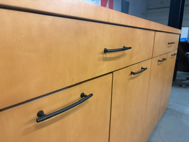 Light wood cabinet drawers with black metal bar handles, shown in a close-up view of the front doors and drawers.